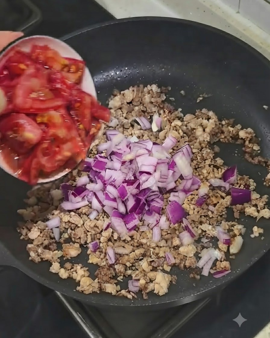 Pomodori freschi a pezzetti aggiunti da una ciotolina nella padella con carne e cipolle.