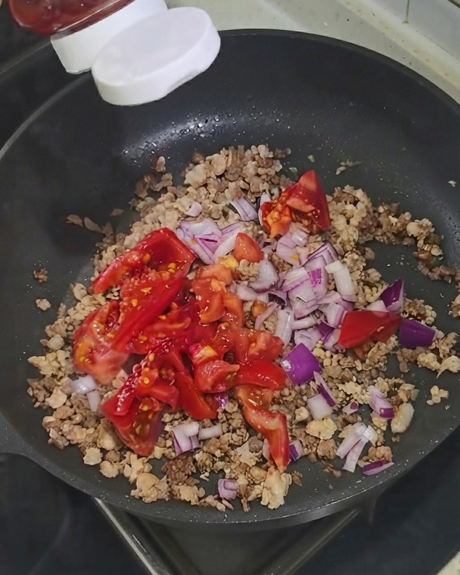 Ketchup spremuto da un flacone direttamente sugli ingredienti nella padella.