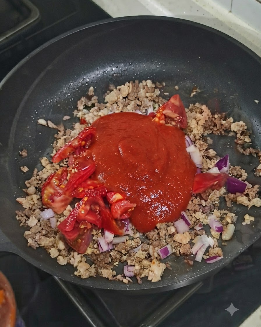 Una cucchiaiata di concentrato di pomodoro sopra il composto di carne e verdure nella padella.