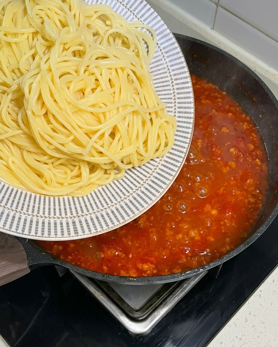 Spaghetti appena bolliti trasferiti da un piatto decorato in una grande padella con un sugo rosso sobbollente.