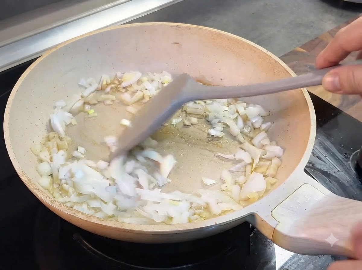 Cipolle tritate mescolate con una spatola grigia in una padella chiara.