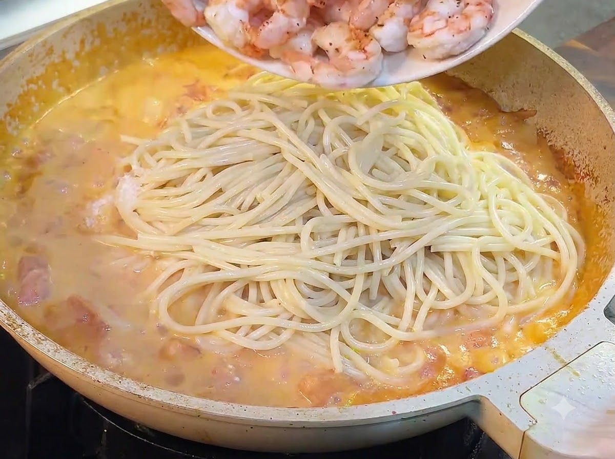 I gamberi cotti vengono versati da un piatto nella padella con spaghetti e sugo.