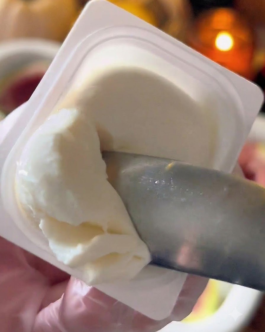 Un coltellino o un cucchiaio che preleva formaggio labneh bianco da un contenitore.