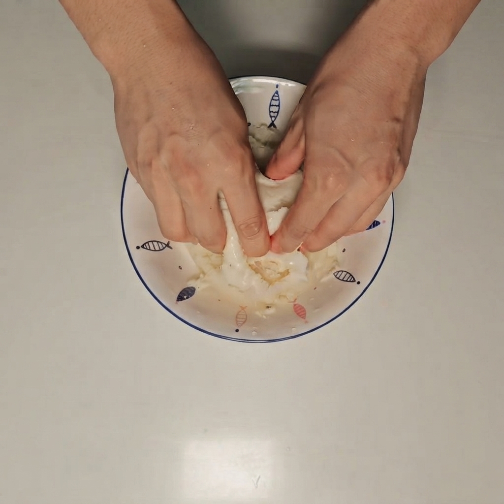 Mani che schiacciano un panino al vapore bagnato allinterno di una ciotola bianca.