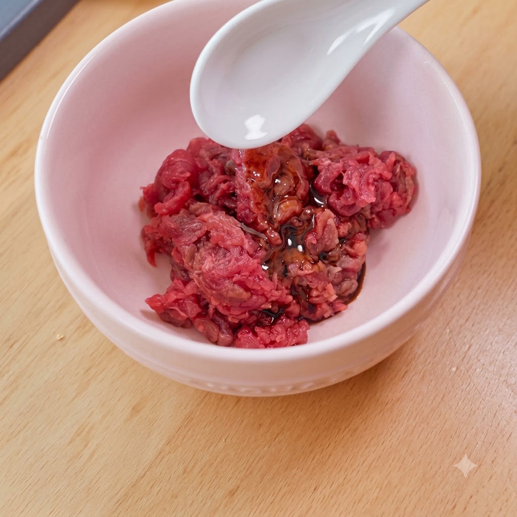 Un cucchiaio bianco che aggiunge lamido in una ciotola rosa piena di manzo crudo a cubetti, salsa di soia e olio.