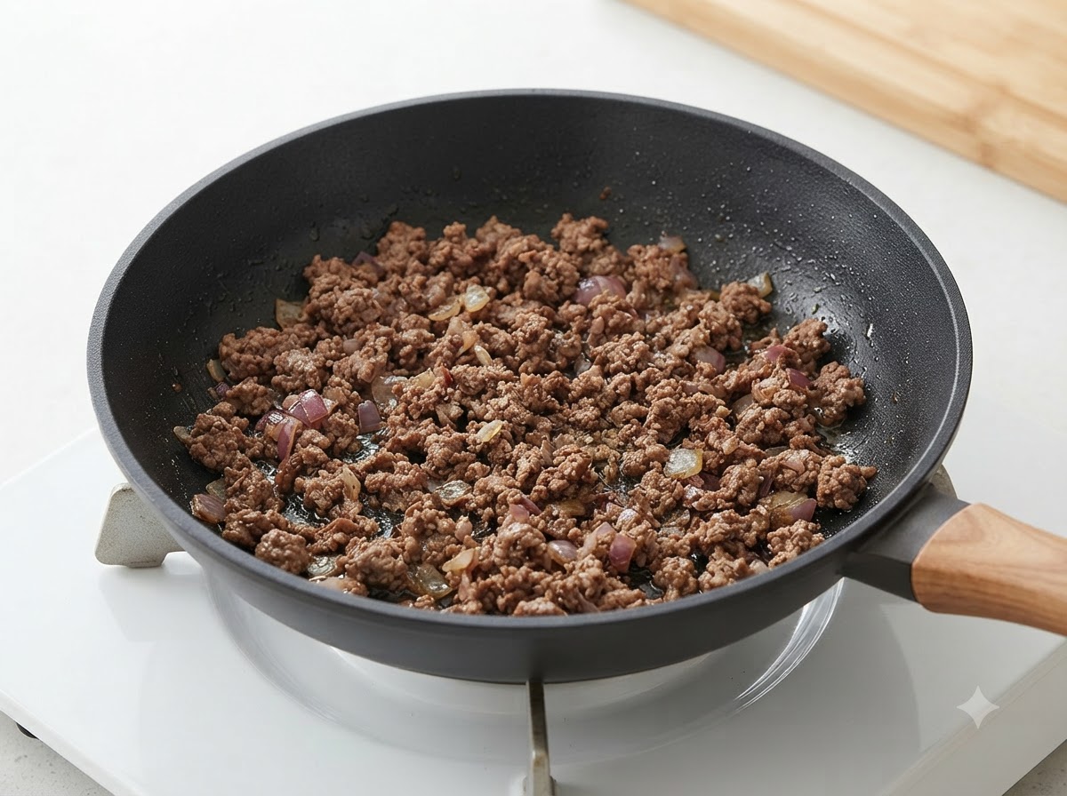 Manzo macinato cotto e cipolle mescolati insieme allinterno di una padella.