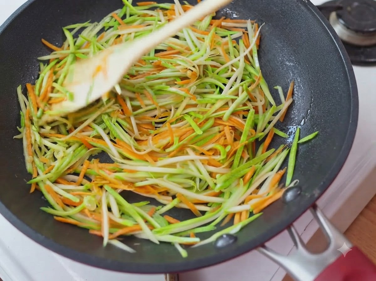 Strisce di zucchine e carote distribuite uniformemente in uno strato circolare allinterno della padella.