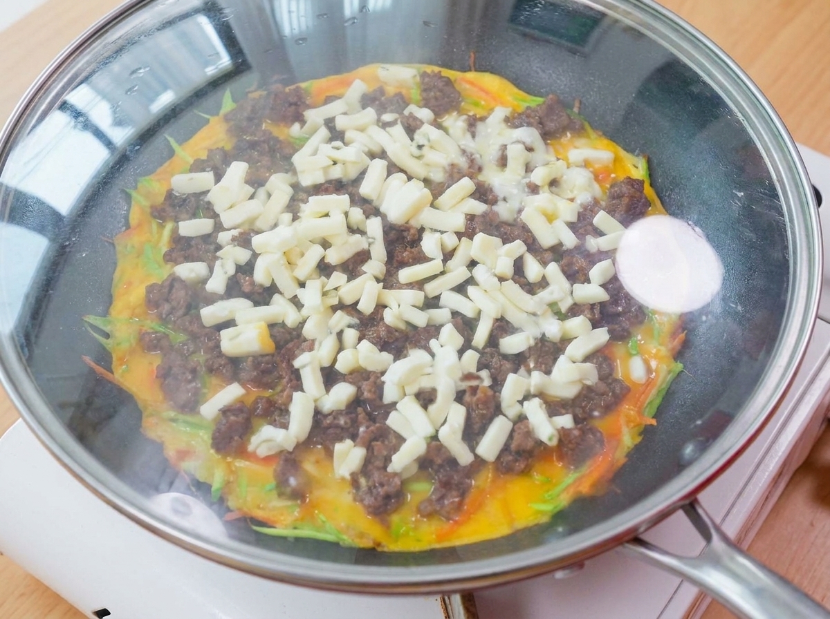 Una padella coperta da un coperchio di vetro su un fornello, con vapore e formaggio fuso visibili allinterno.