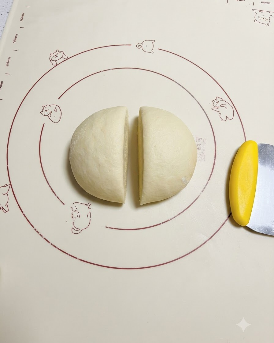 Impasto lievitato tagliato uniformemente a metà su un tappetino in silicone decorato accanto a un tarocco giallo.