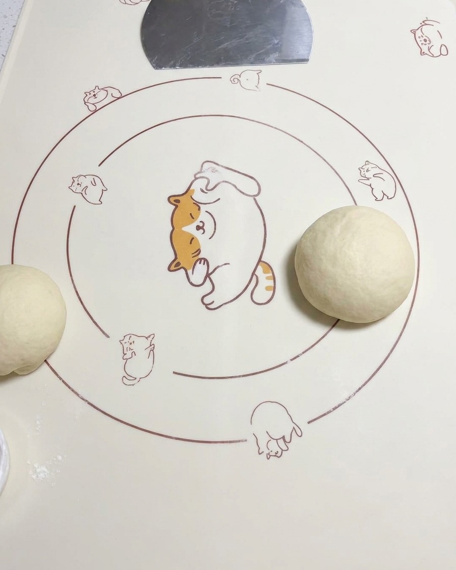 Una pallina di impasto arrotondata appoggiata su un tappetino in silicone accanto a un altro pezzo di impasto steso.