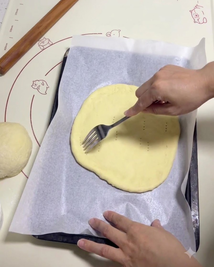 Una mano che usa una forchetta di metallo per fare piccoli buchi su un pezzo di impasto per pizza piatto e rotondo su carta da forno.
