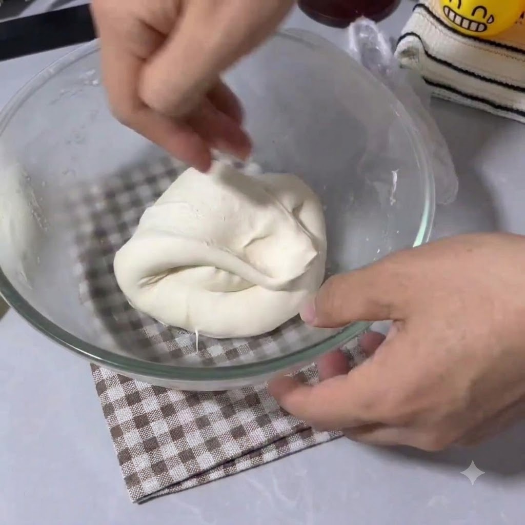 Mani che piegano e stendono un impasto per pizza elastico allinterno di una ciotola trasparente.