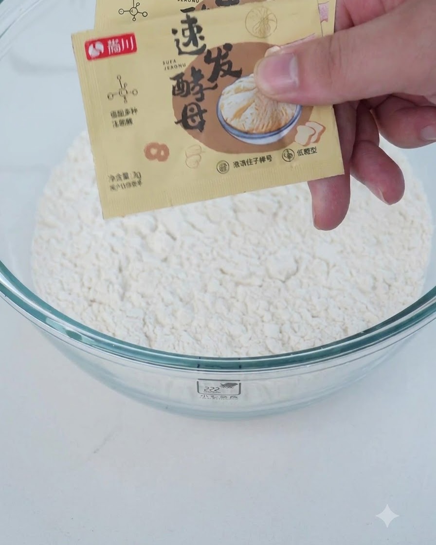 Ingredienti secchi e liquidi, tra cui farina e lievito, versati in una ciotola di vetro trasparente.