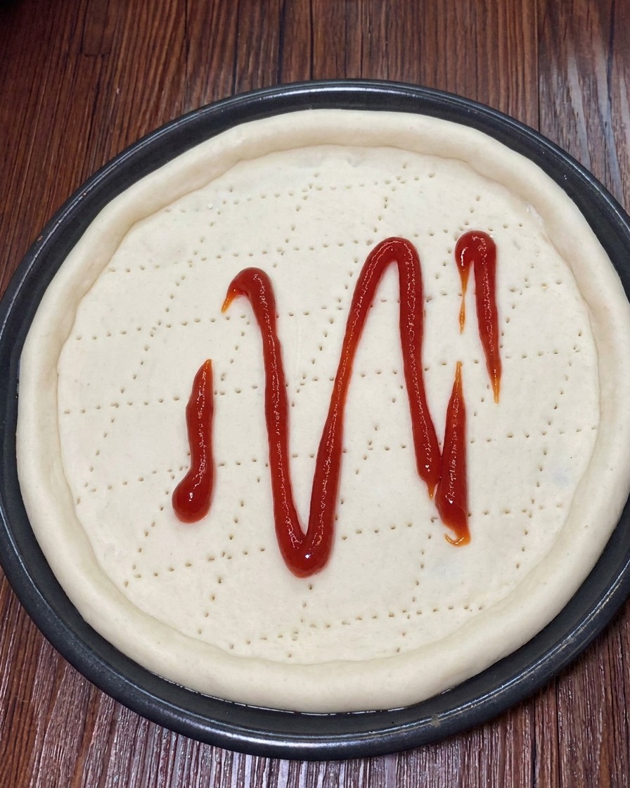 Mozzarella grattugiata cosparsa uniformemente sopra la salsa di pomodoro sulla pizza.