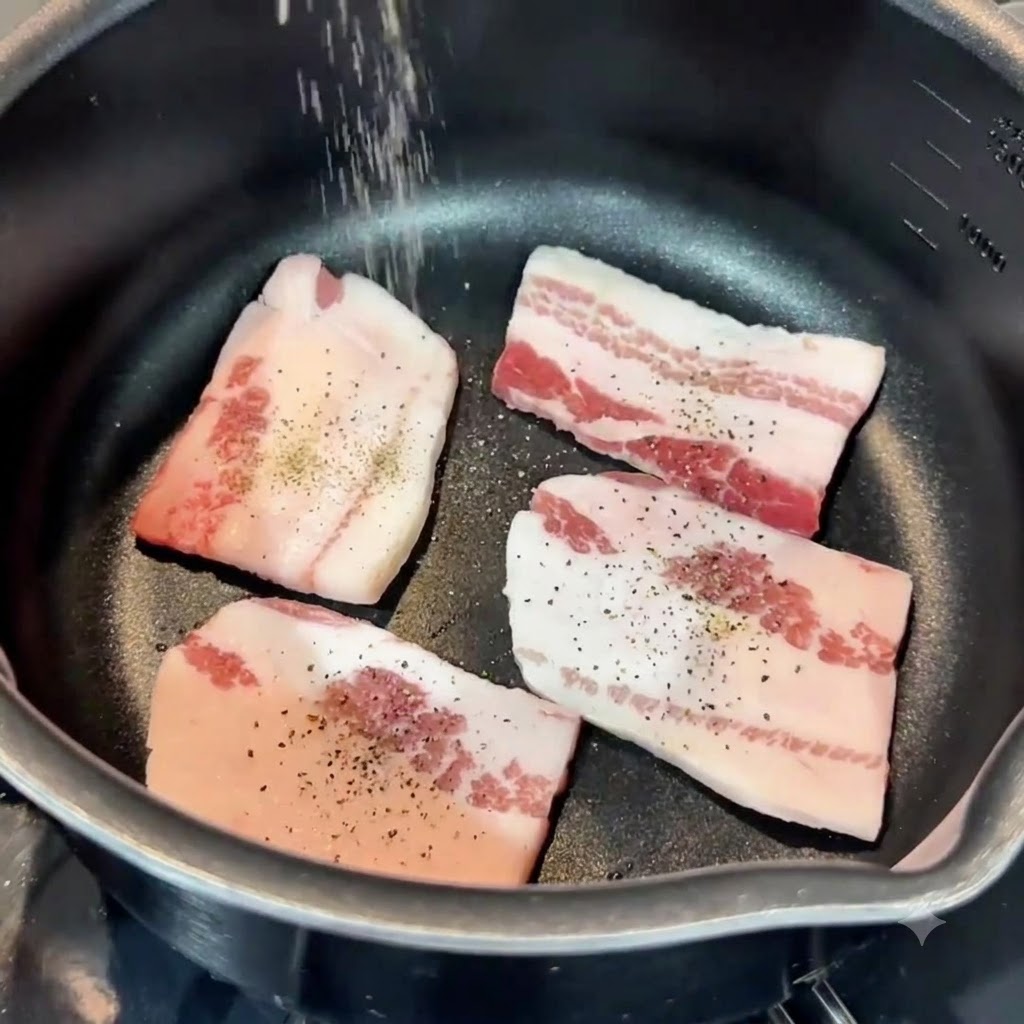 Sale e pepe cosparsi dallalto sulle fette di pancetta di maiale allinterno di una padella.