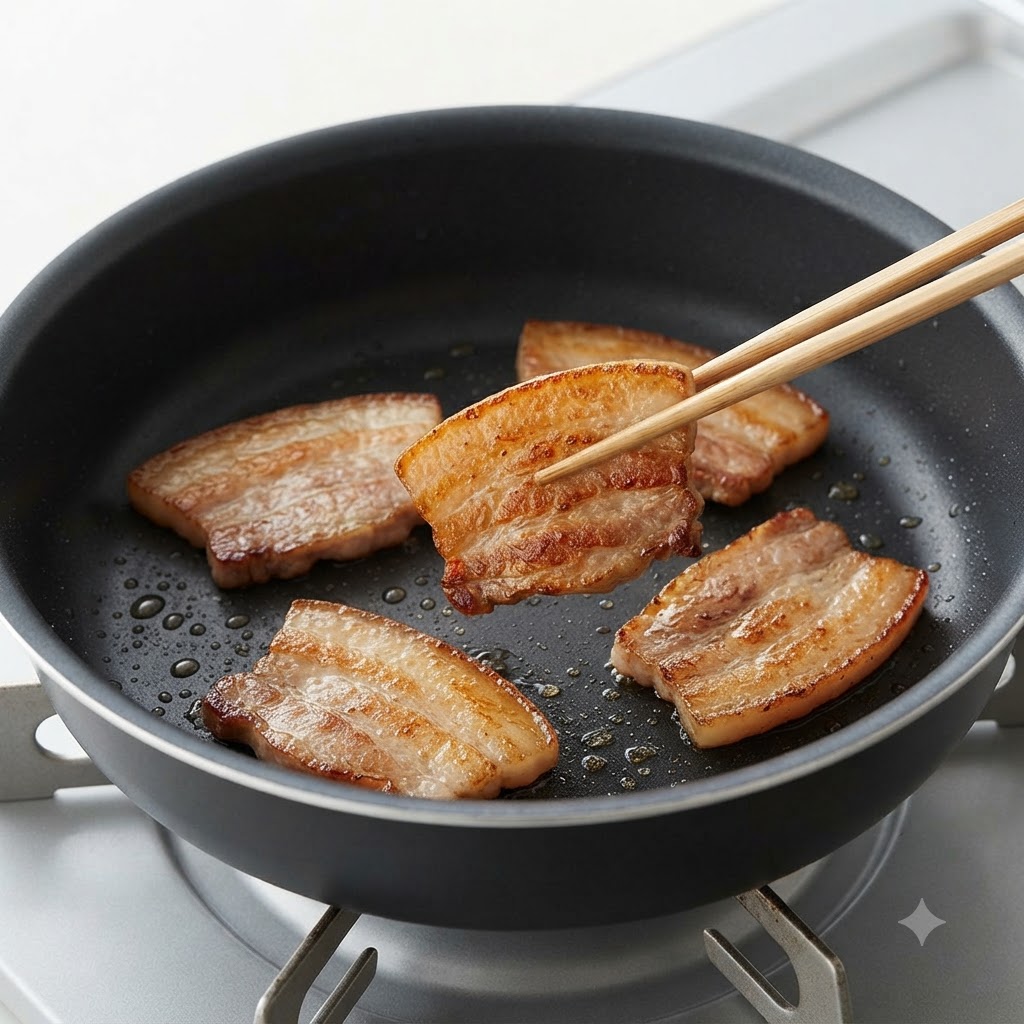 Un paio di bacchette che girano una fetta di pancetta di maiale dorata e scottata in una padella.