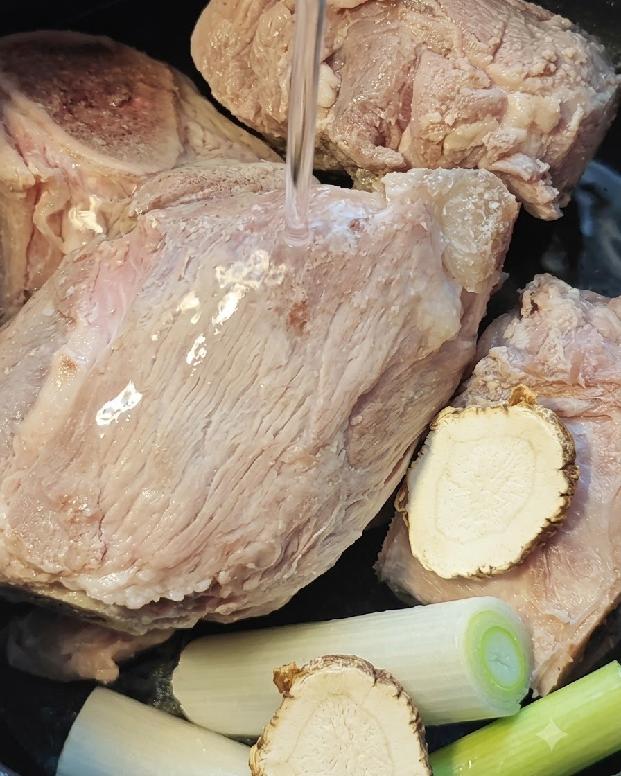 Acqua versata sopra le ossa di maiale, la radice di angelica e i cipollotti allinterno di una pentola da cuociriso.