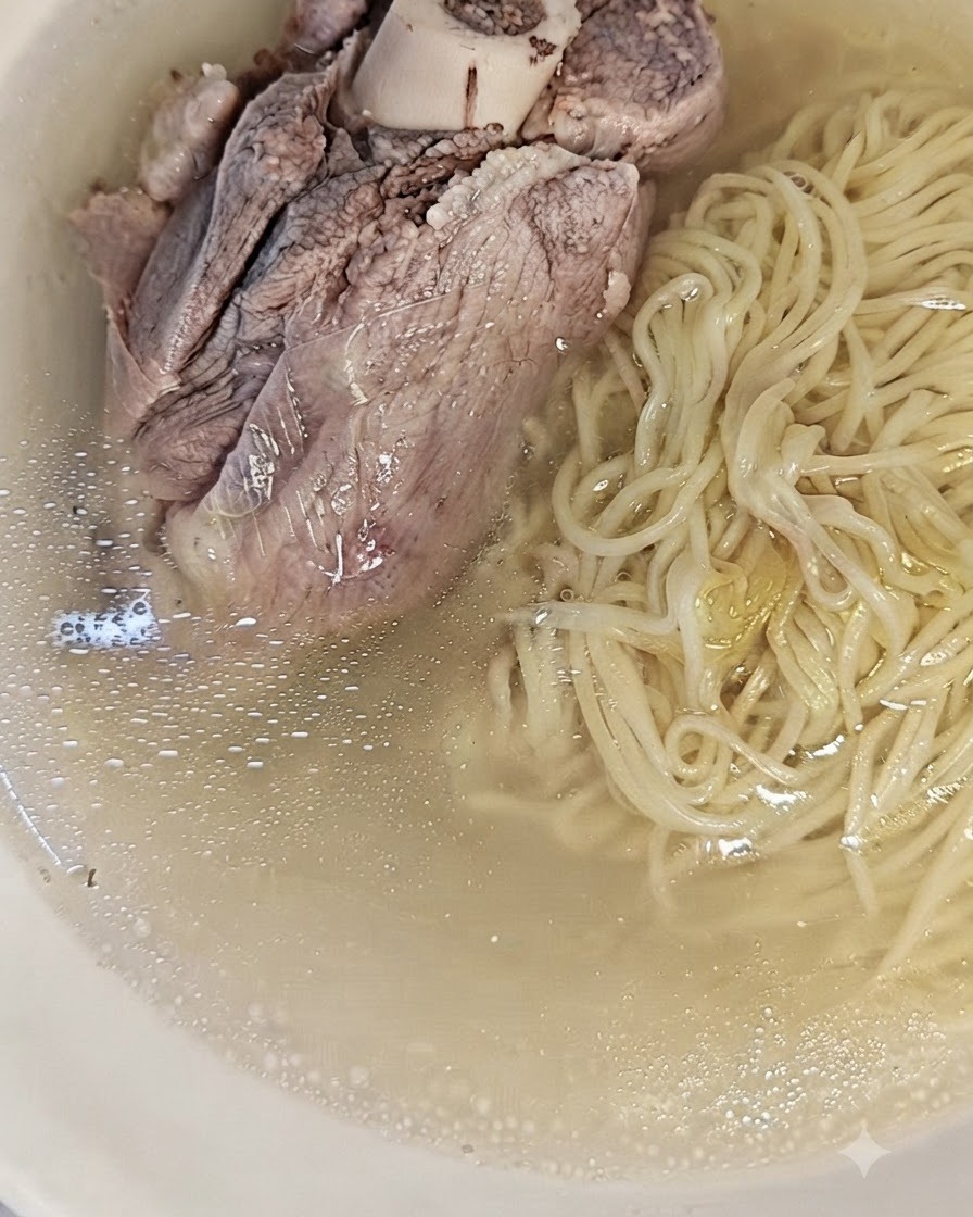Noodles cotti in una ciotola accanto al brodo di maiale chiaro e filtrato.