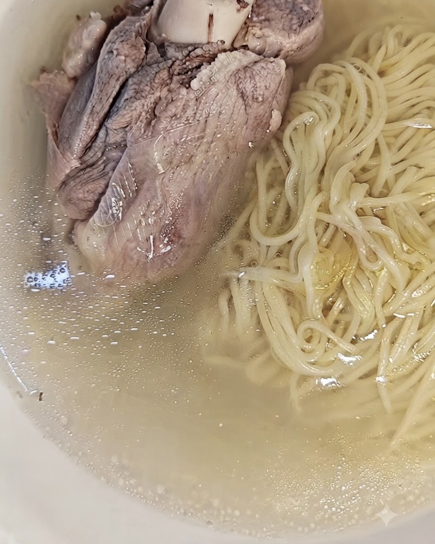 Un grande osso di maiale cotto posizionato sopra i noodles e il brodo in una ciotola, pronto per essere servito.