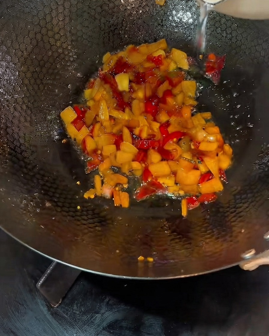 Brodo liquido versato nella padella contenente il miscuglio di verdure sottaceto cotte.