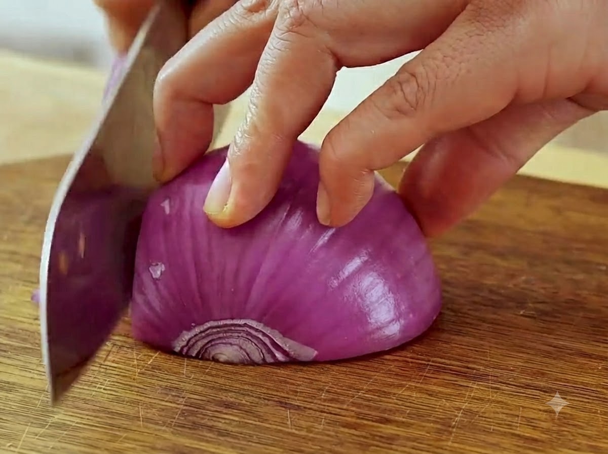 Mani che tengono un coltello e affettano una cipolla rossa in strisce sottili su un tagliere.
