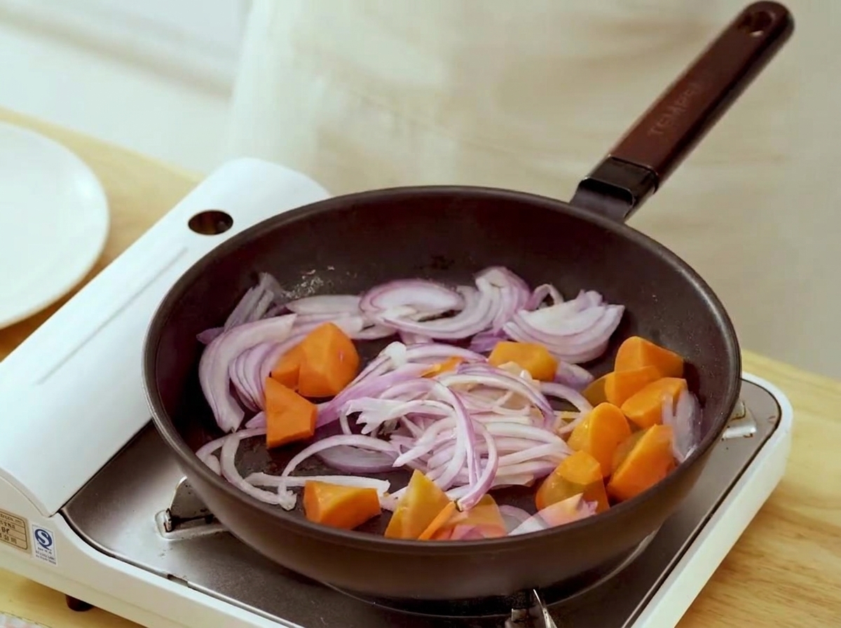 Pezzi di carota e strisce di cipolla che sobbollono in una padella.