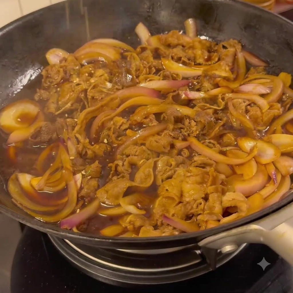 Manzo e cipolle che sobbollono in una scura salsa teriyaki in una padella.