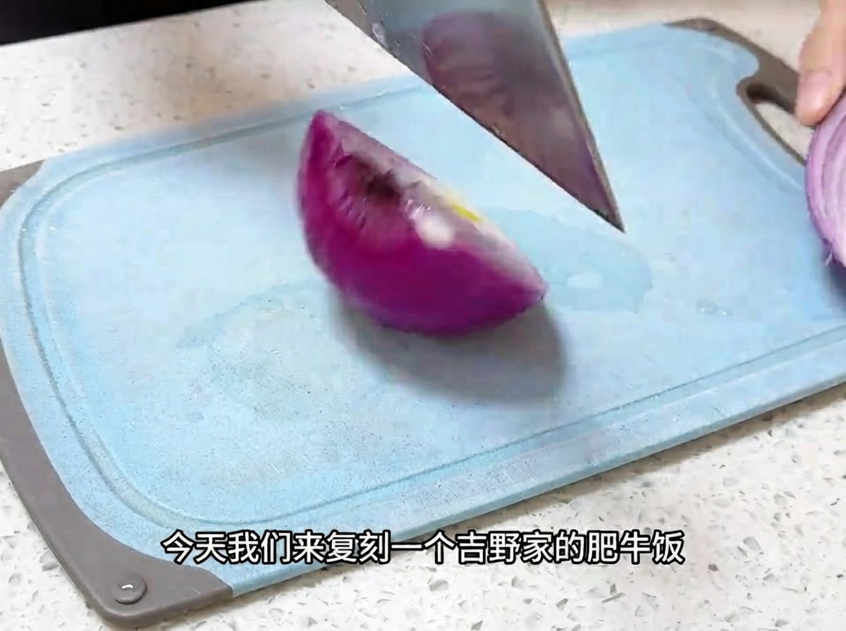 Un coltello da cucina che affetta una cipolla rossa in pezzi sottili su un tagliere blu.