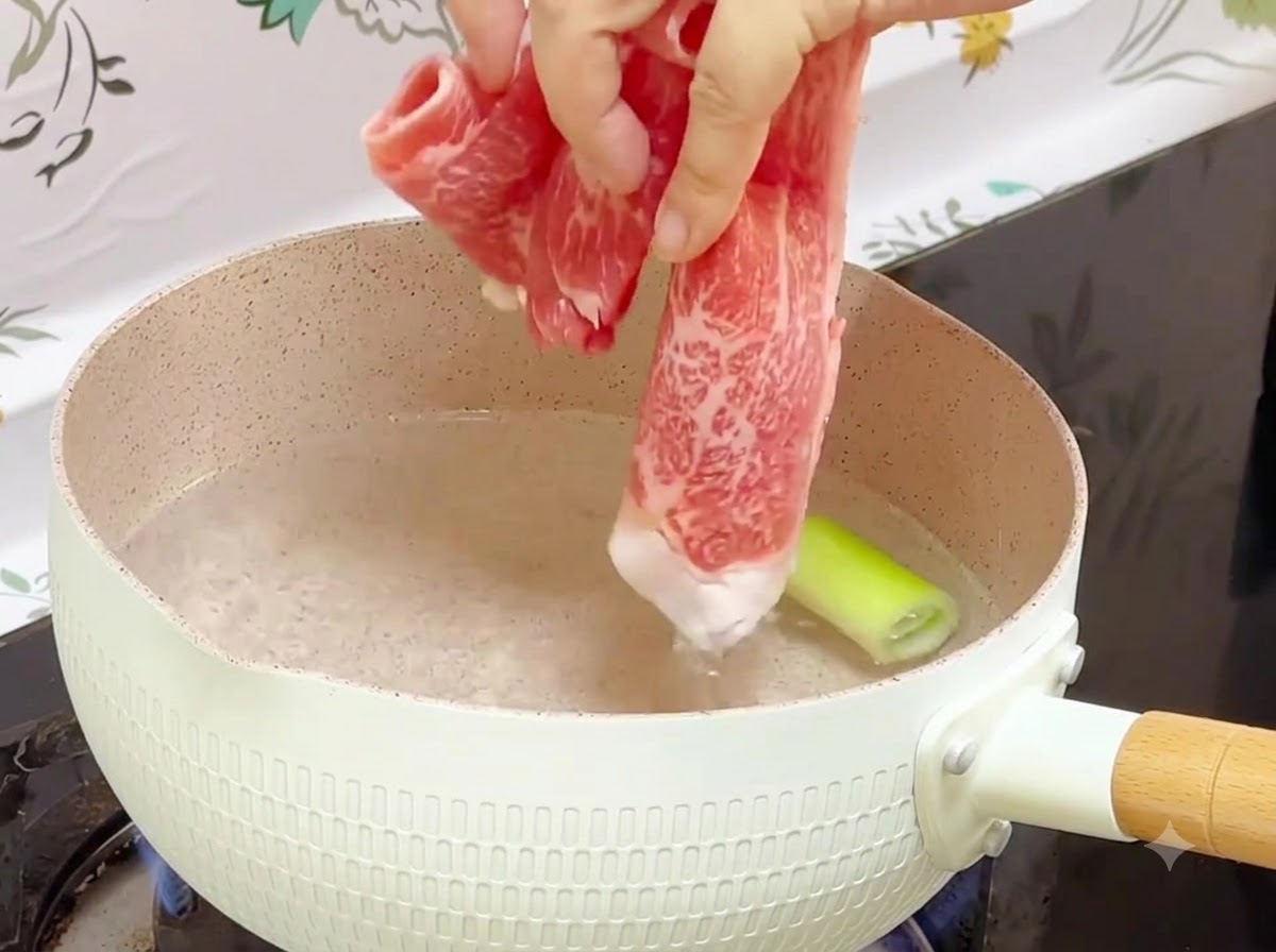 Involtini di manzo congelati immersi in una pentola di acqua bollente con un pezzo di cipollotto allinterno.