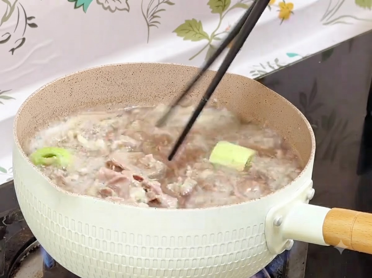 Bacchette che recuperano gli involtini di manzo sbollentati da una pentola bollente in un contenitore.