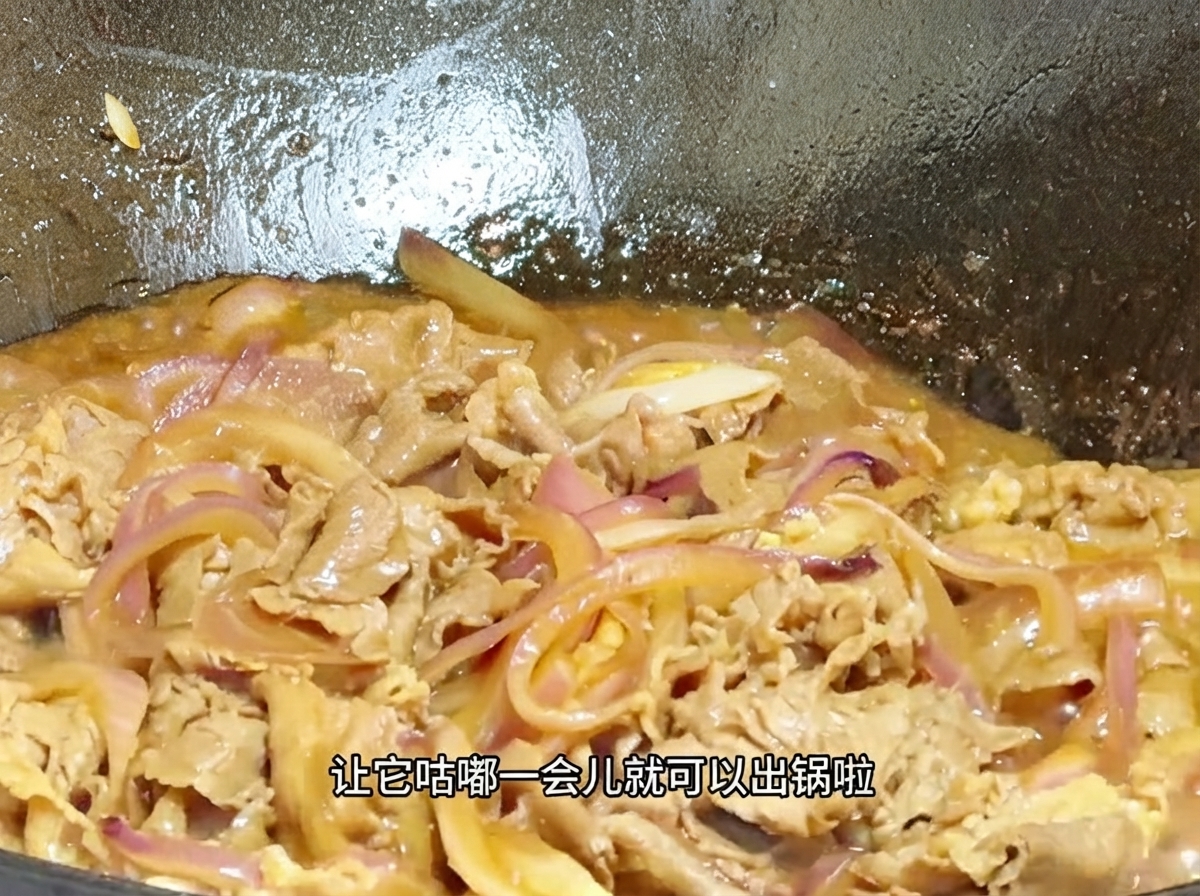 Una vista ravvicinata di manzo e cipolle che sobbollono in una salsa densa e frizzante allinterno di un wok.