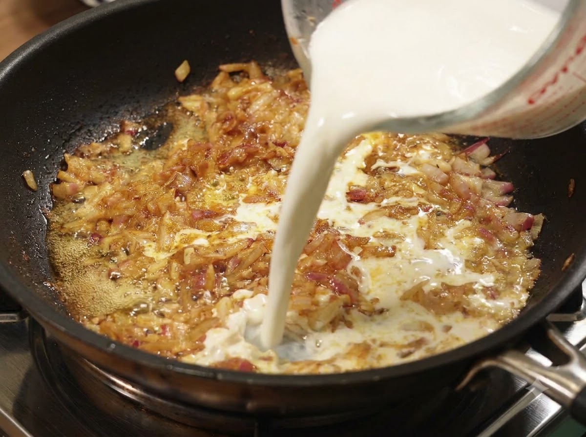 Latte versato da un misurino in una padella di cipolle e curry in ebollizione.