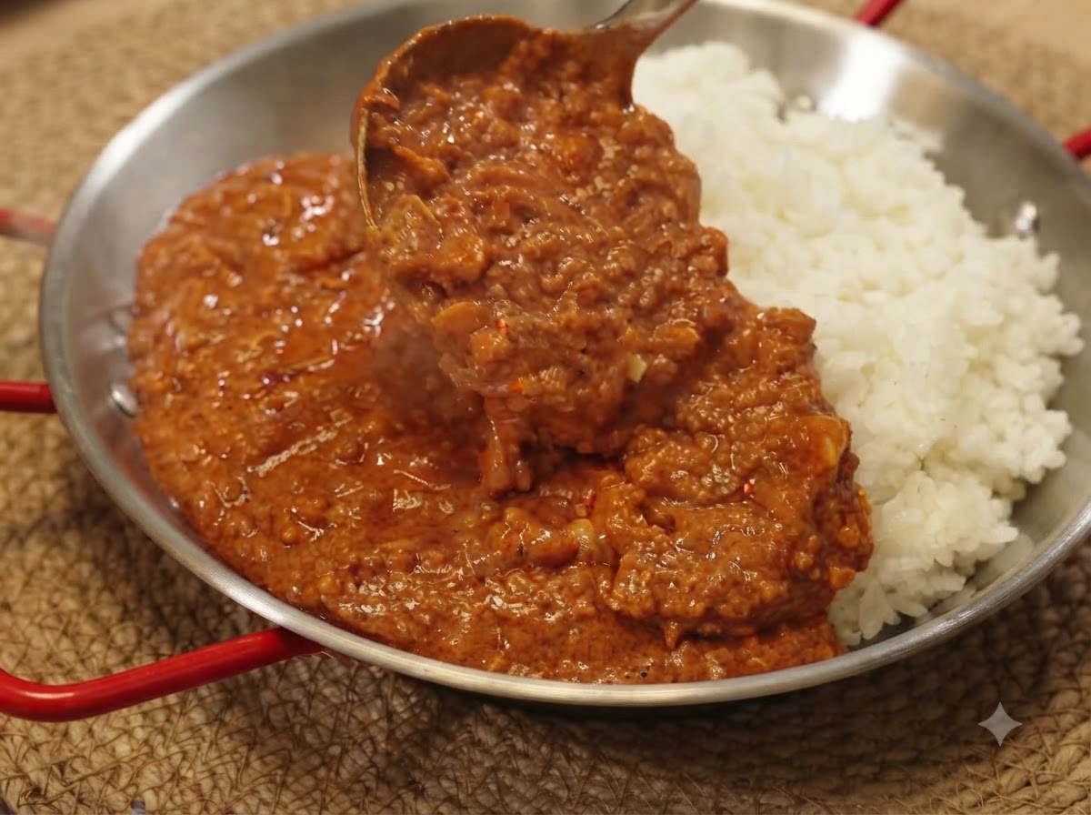 Un mestolo che raccoglie la ricca salsa di maiale macinato al curry su un letto di riso bianco in una padella di portata.
