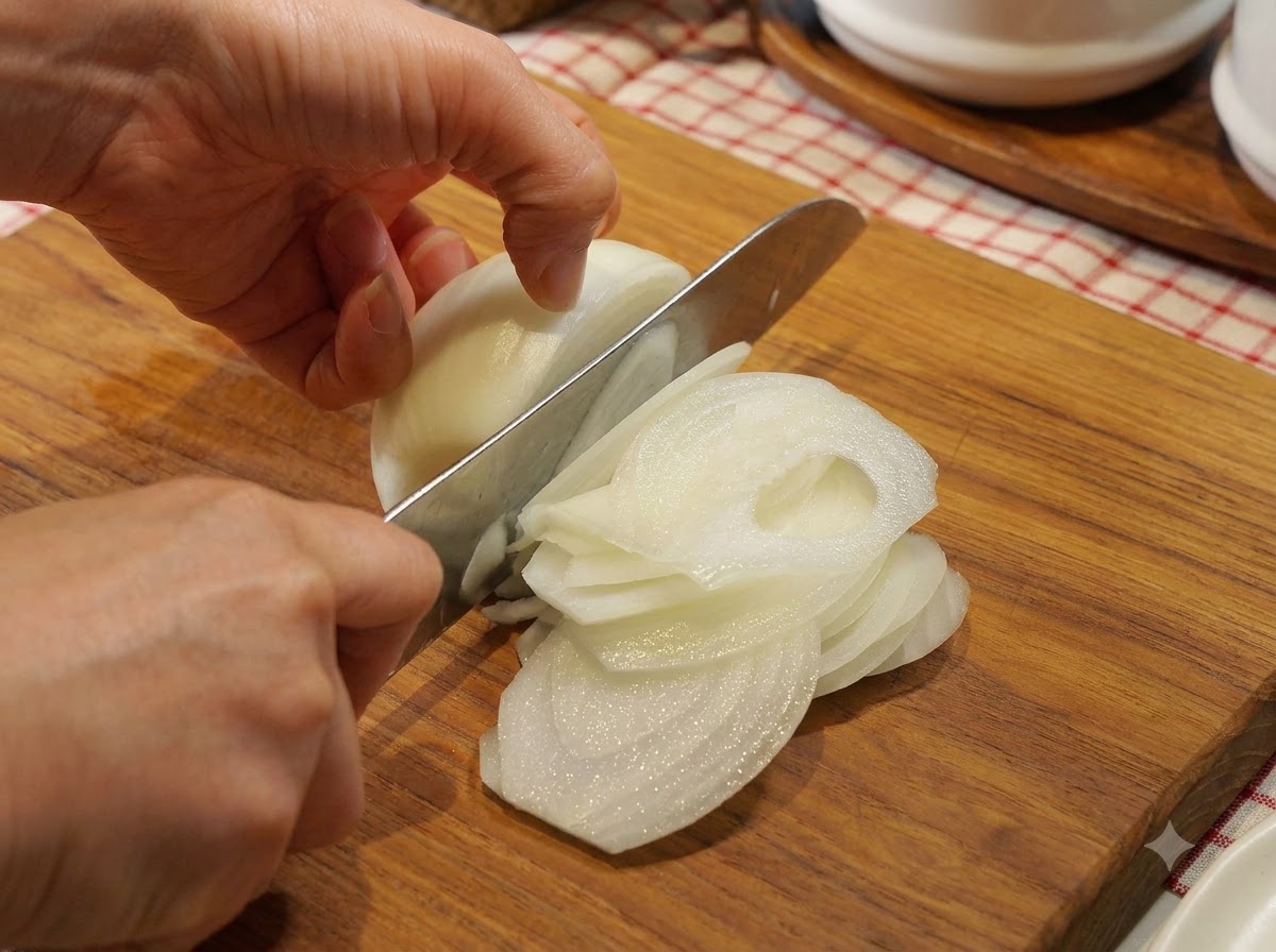 Una cipolla tagliata con cura a fettine sottili a mezzaluna su un tagliere di legno con un coltello da cucina.