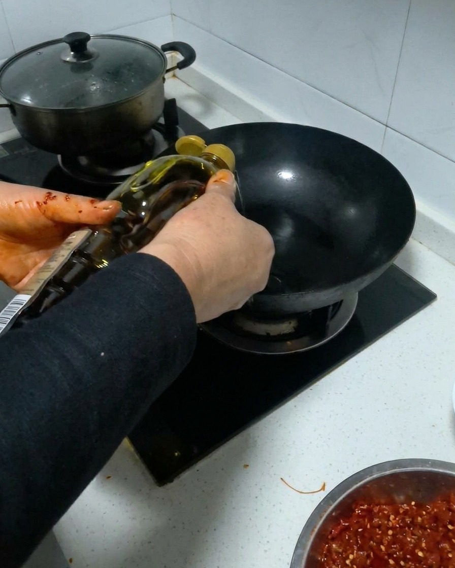 Olio da cucina versato da una bottiglia in un wok nero riscaldato.