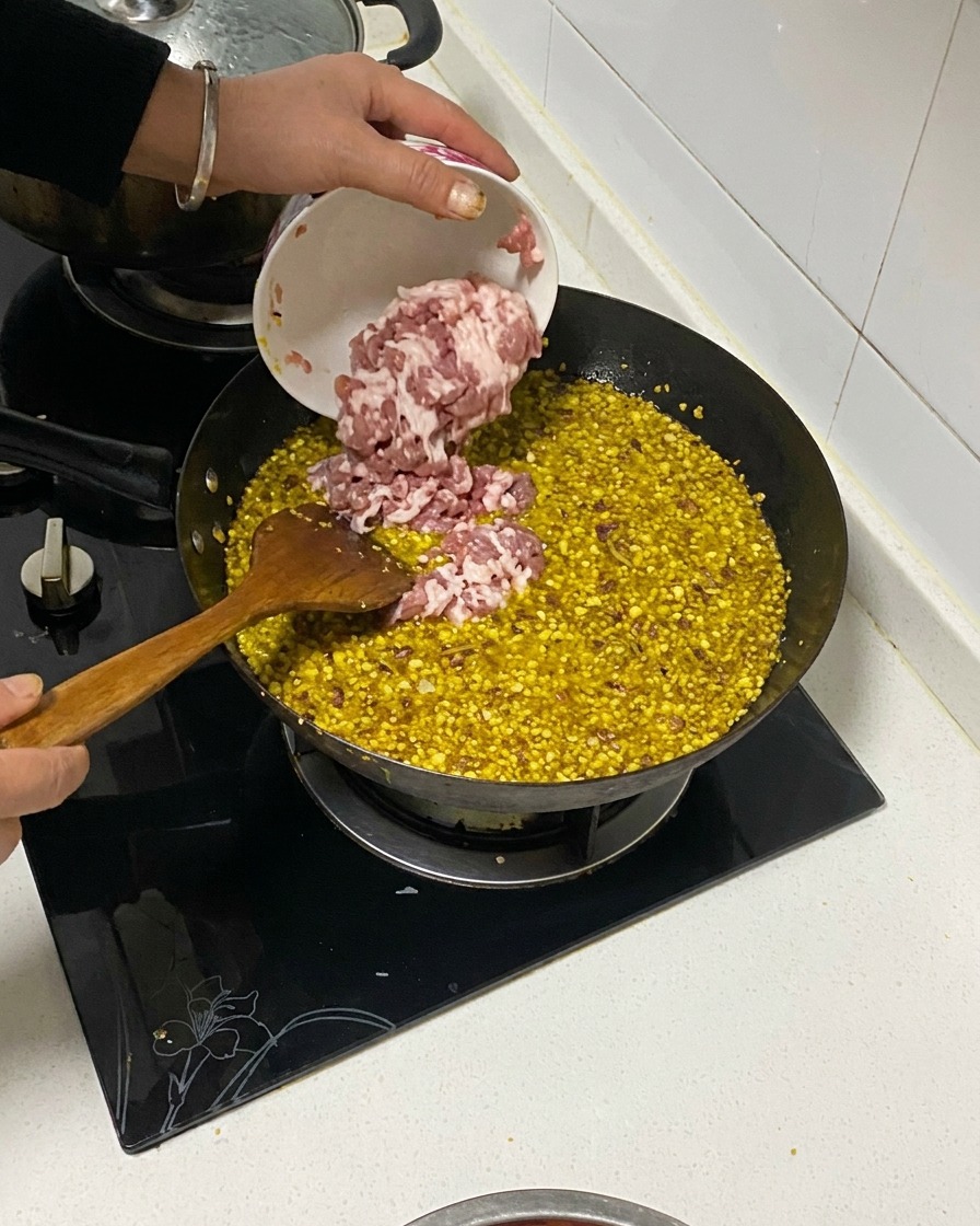 Pancetta di maiale a dadini versata da una ciotolina in un wok contenente aromi fritti e olio.