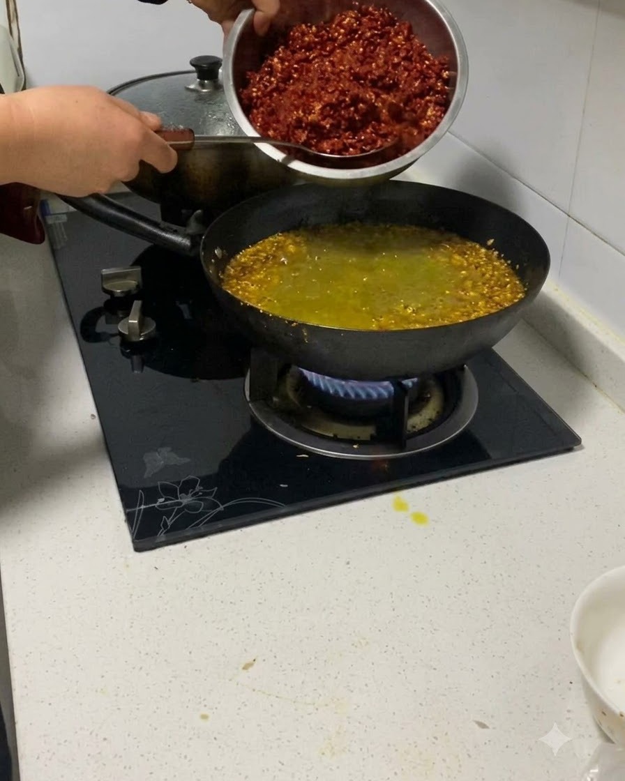 Peperoncini rossi tritati aggiunti da una ciotola di metallo in un wok con carne e aromi.
