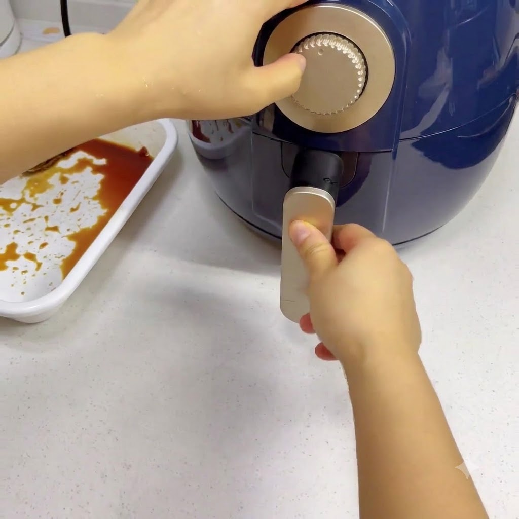 Una mano che gira la manopola del timer argentata su una friggitrice ad aria blu scuro.