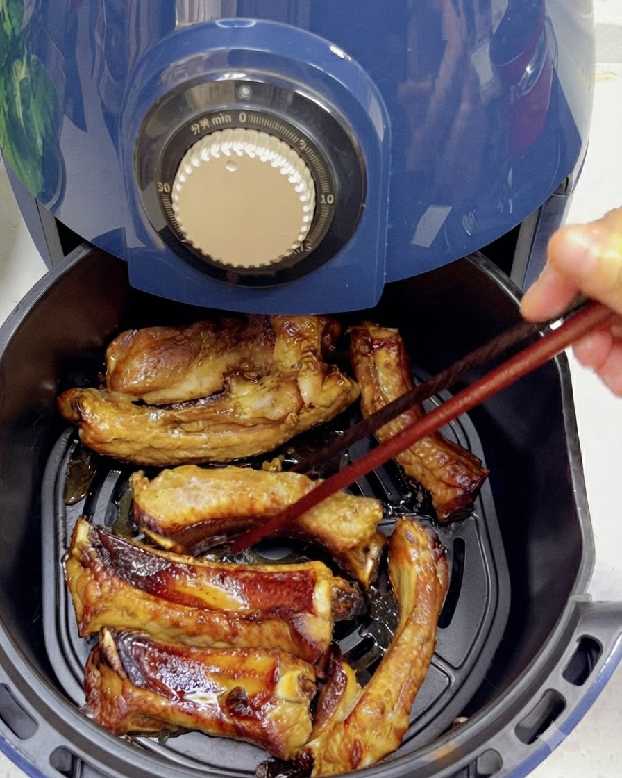 Utilizzo di bacchette per girare costine di maiale parzialmente cotte e dorate allinterno di un cestello per friggitrice ad aria.