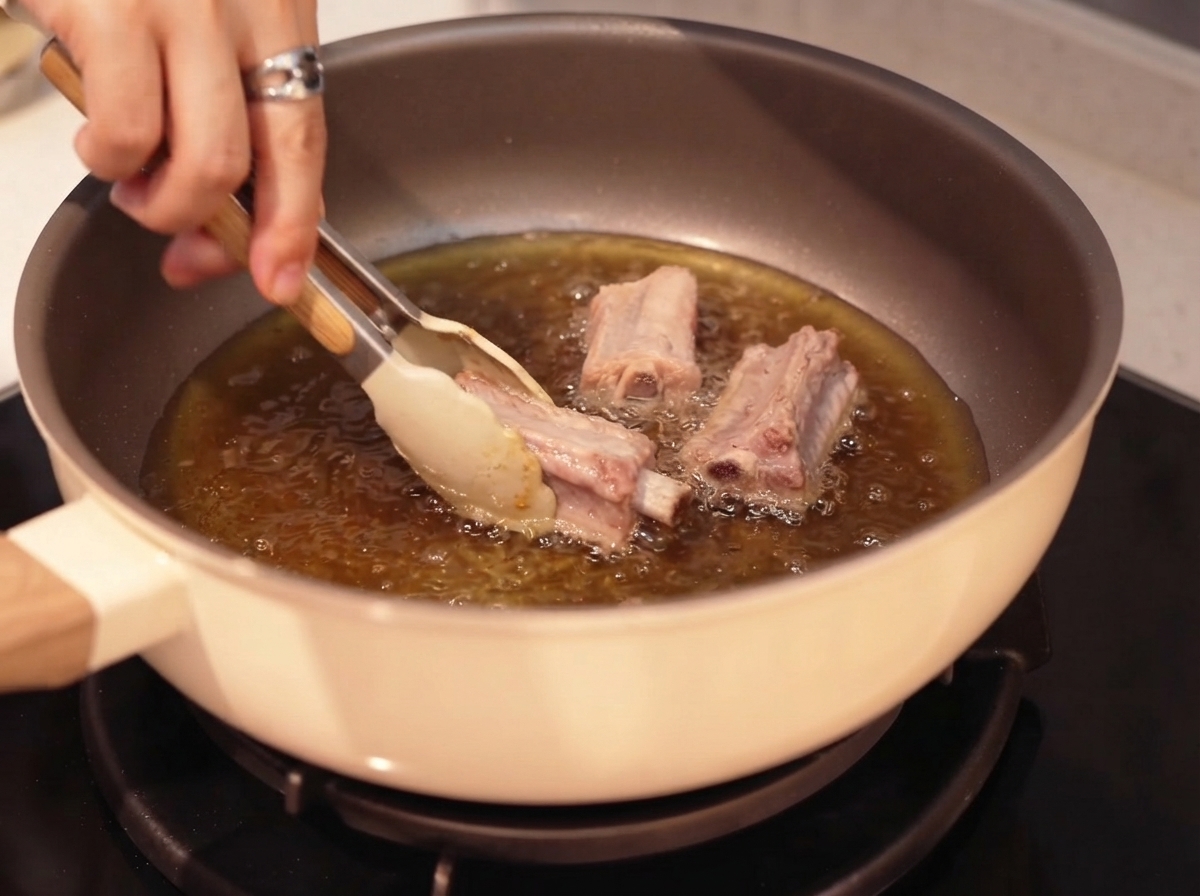 Costine di maiale rosolate in olio caldo con laiuto di una pinza.
