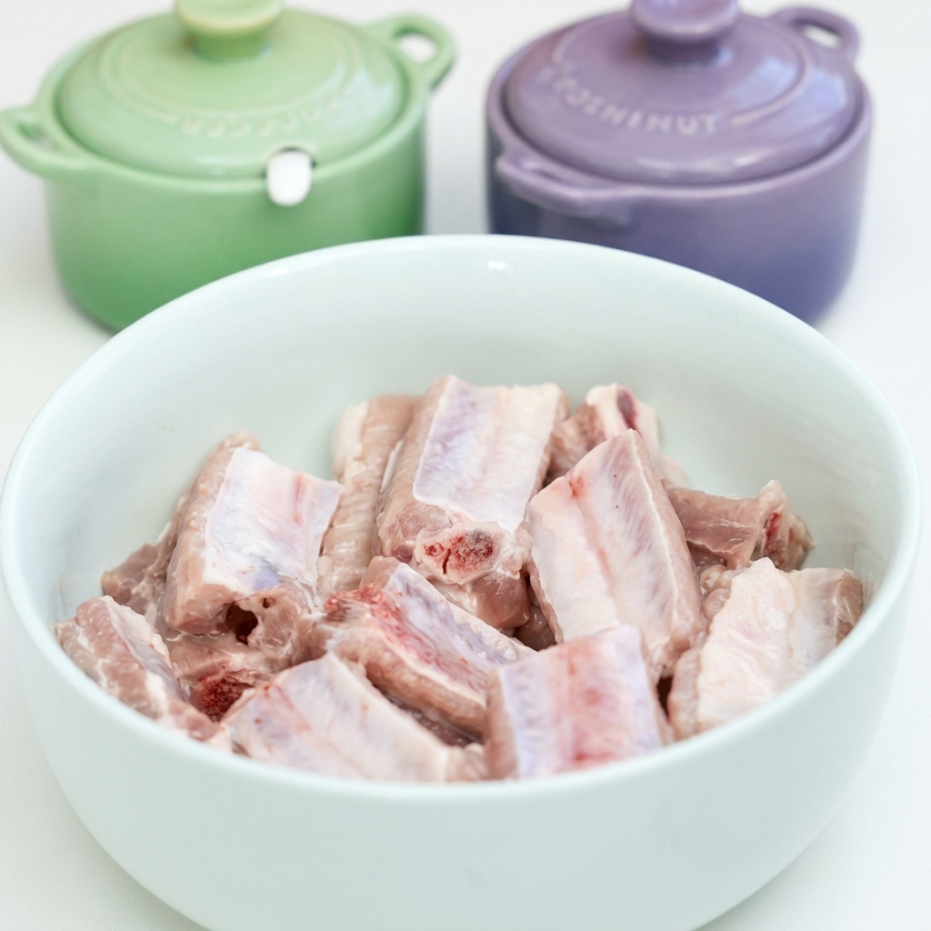 Costine di maiale crudi in una ciotola bianca condite con aglio, salse di soia, salsa dostriche e spezie.
