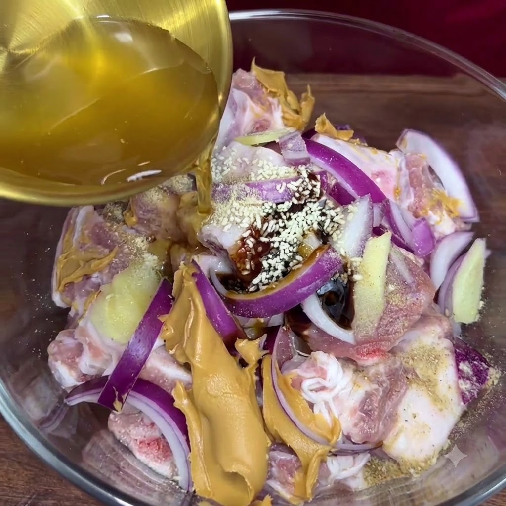 Succo daglio dorato versato da un mettiliquido nella ciotola di vetro contenente le costine di maiale condite e gli altri ingredienti della marinata.