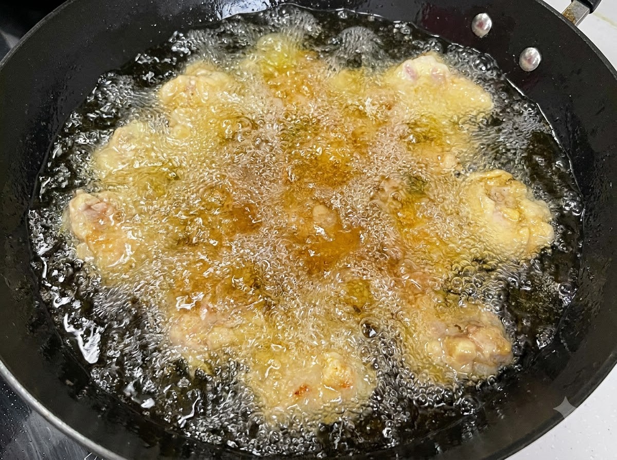 Più pezzi di costine di maiale che friggono in olio caldo e bollente allinterno di un wok nero.
