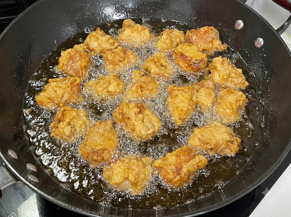 Pezzi di costine di maiale rivestite che friggono in un wok nero pieno di olio bollente.