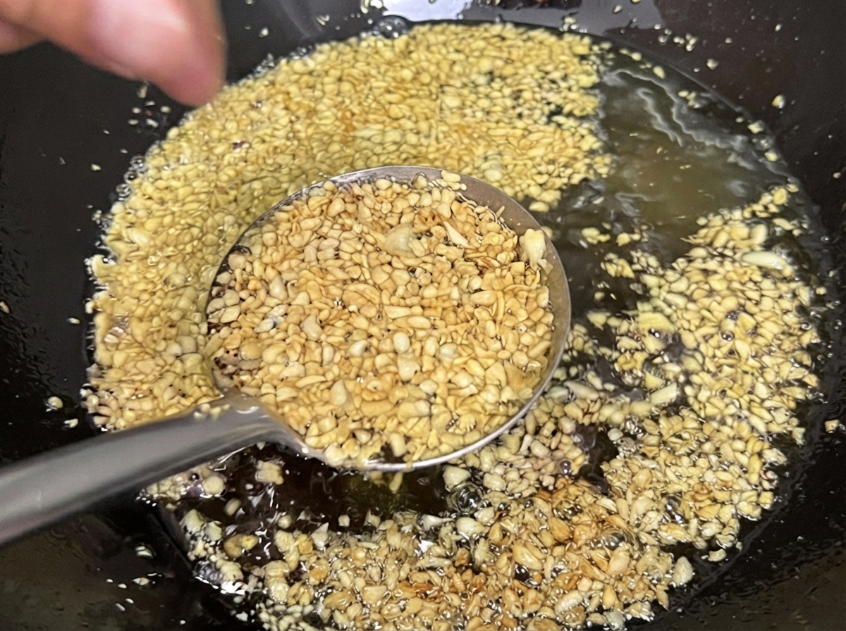Aglio tritato che frigge nellolio allinterno di un wok, diventando giallo dorato chiaro e croccante.