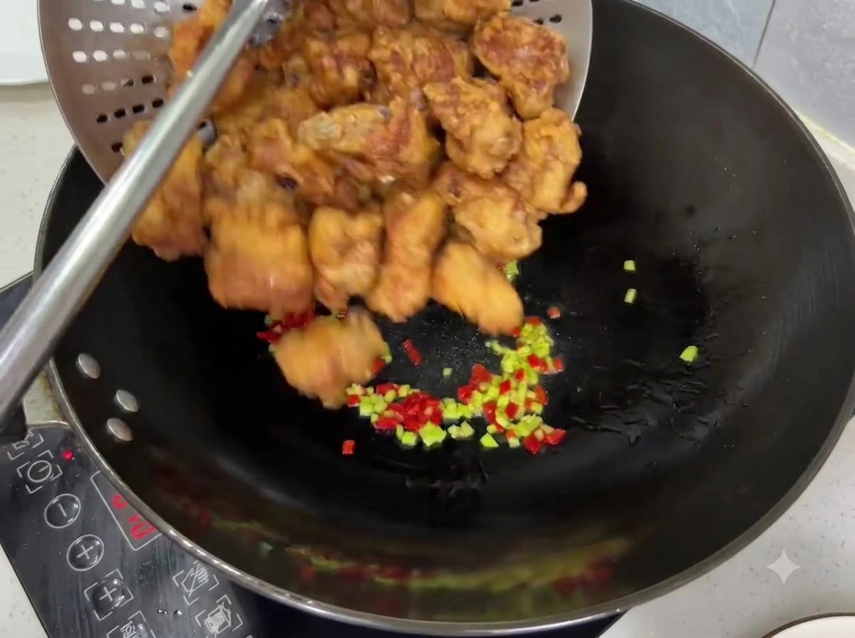 Costine di maiale fritte dorate e croccanti versate da un colino in un wok con i peperoncini.