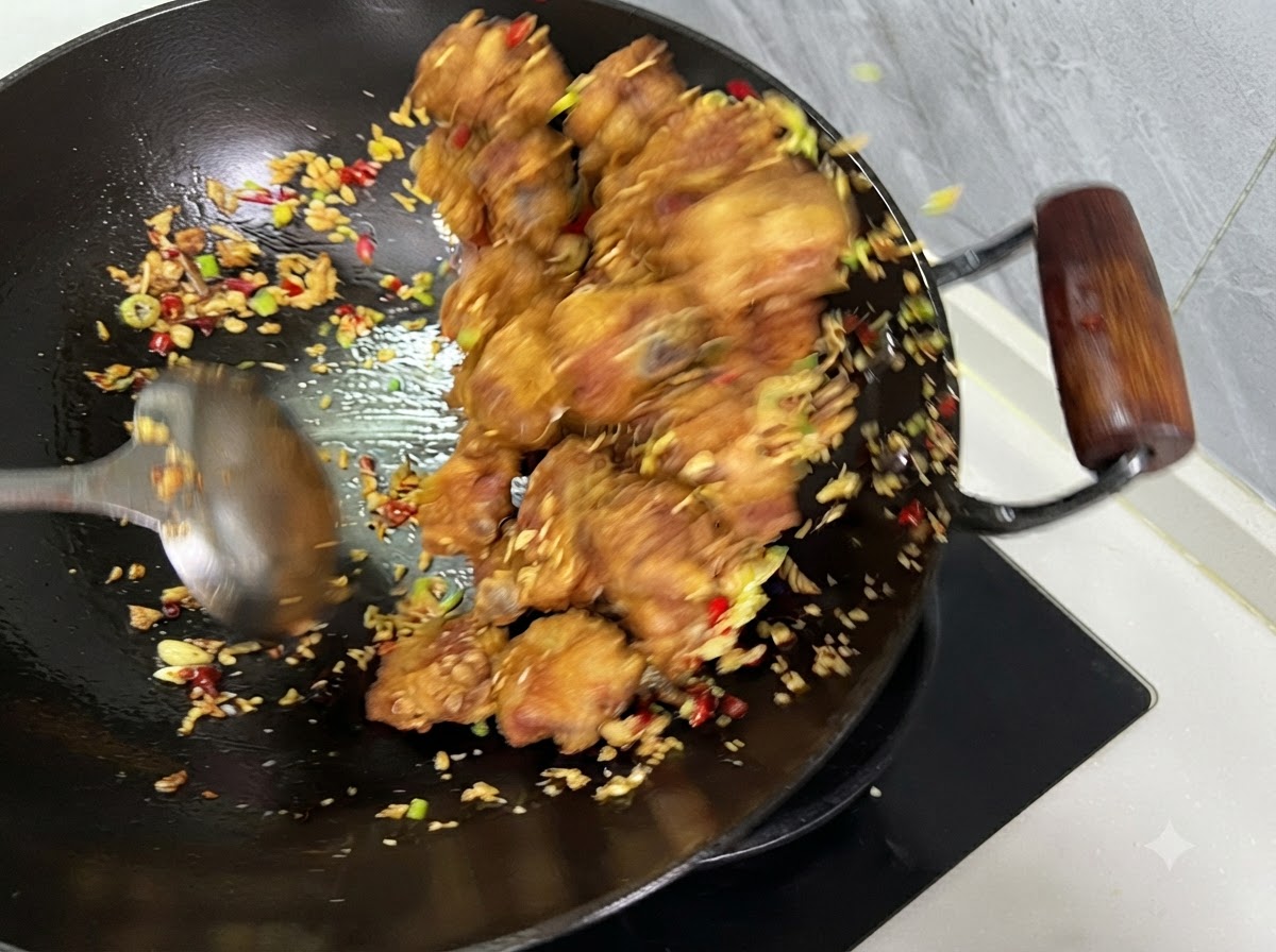 Costine, peperoncini e aglio saltati insieme con un mestolo allinterno di un wok.