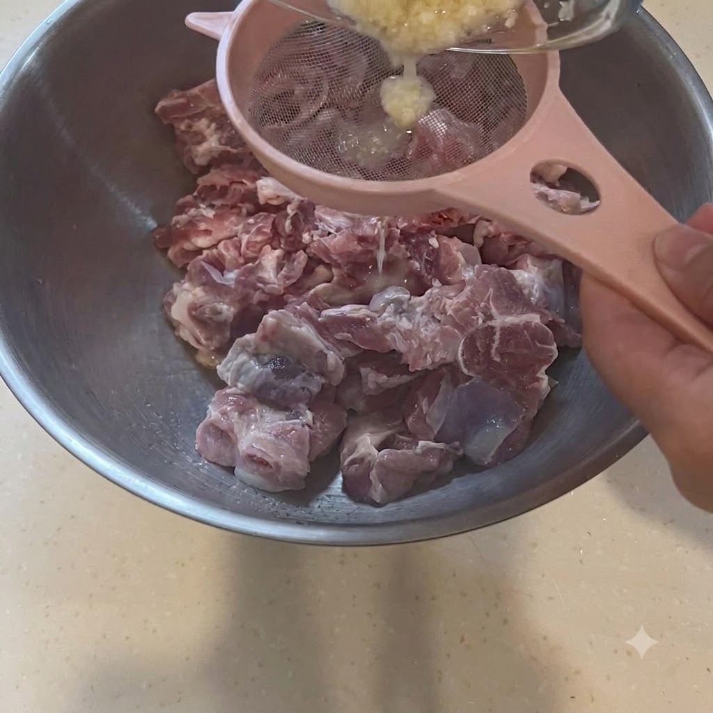 Pasta daglio filtrata attraverso un colino rosa direttamente sopra una ciotola di pezzi di maiale crudo.