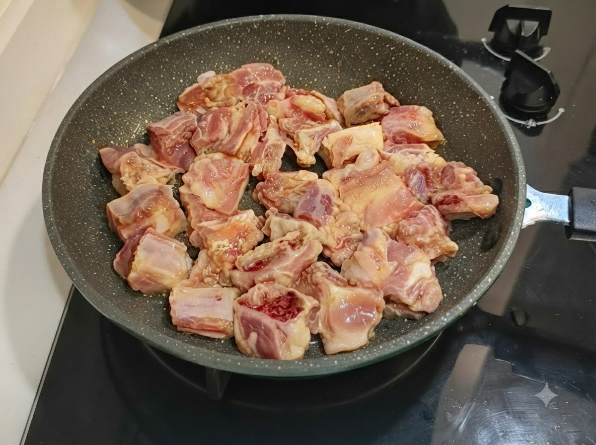Costolette di maiale marinate disposte ordinatamente in una padella maculata su un piano cottura.