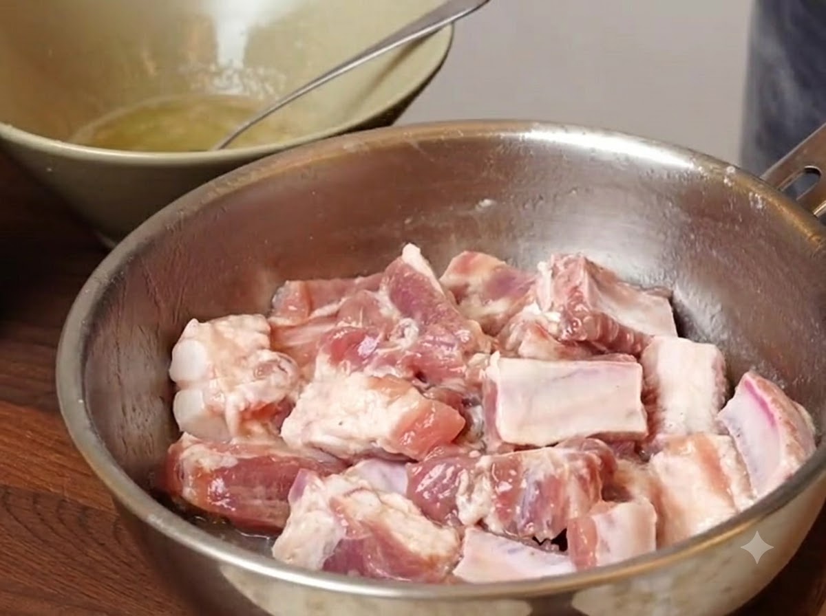 Pezzi di costine di maiale in una ciotola di metallo con condimenti e amidi aggiunti prima di essere mescolati.